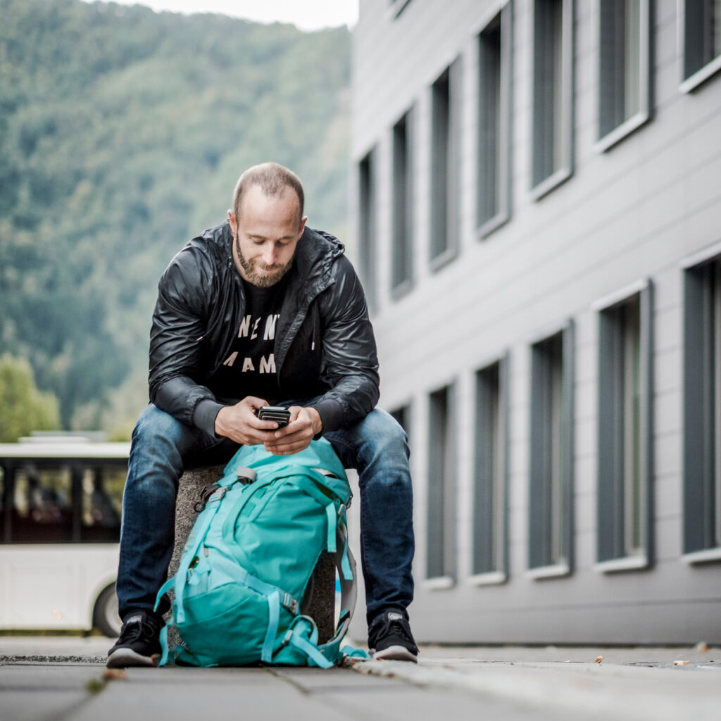 En mann utendørs som sitter og ser på mobiltelefonen sin. 